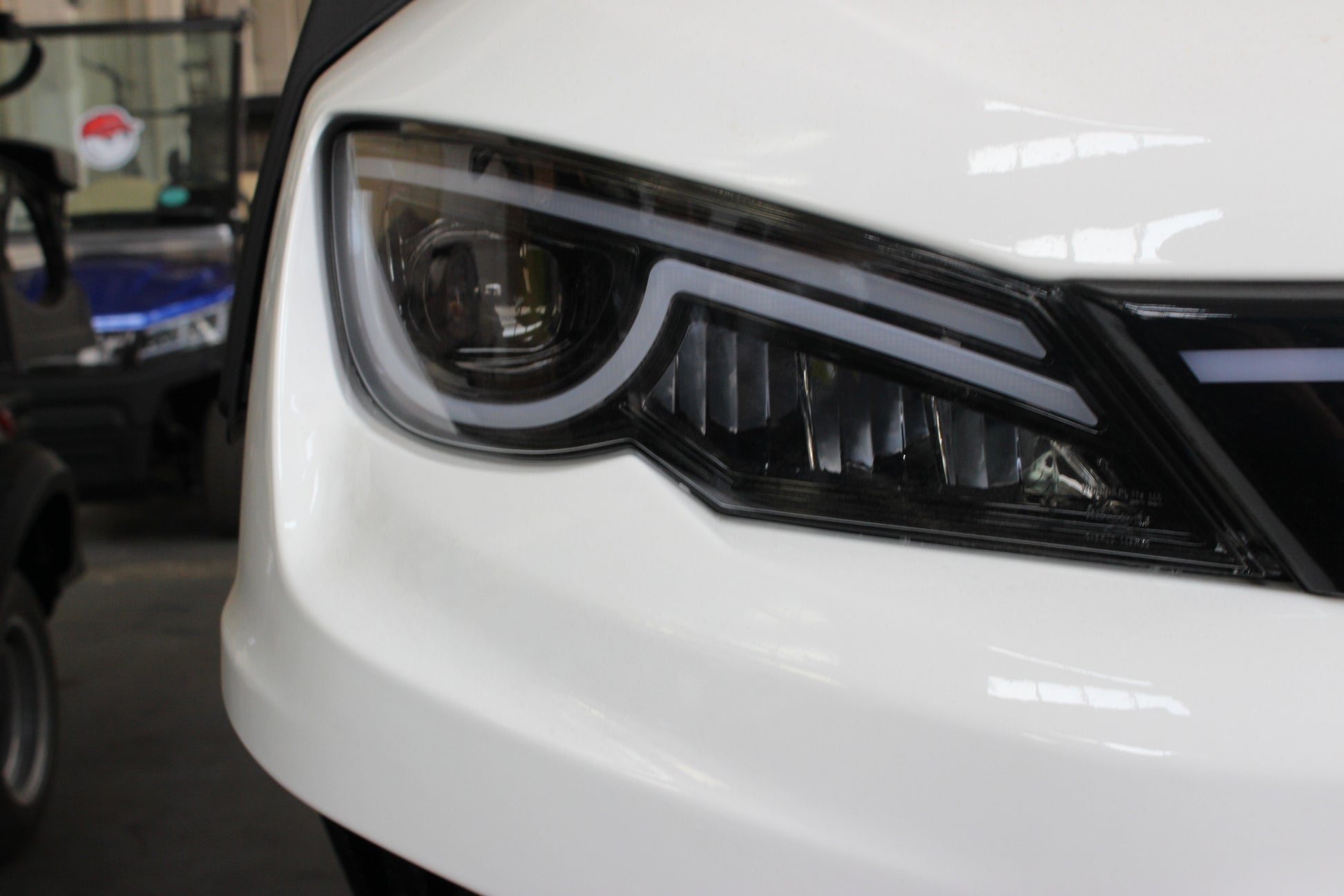 Close-up of a headlight on a white electric golf cart in a showroom setting