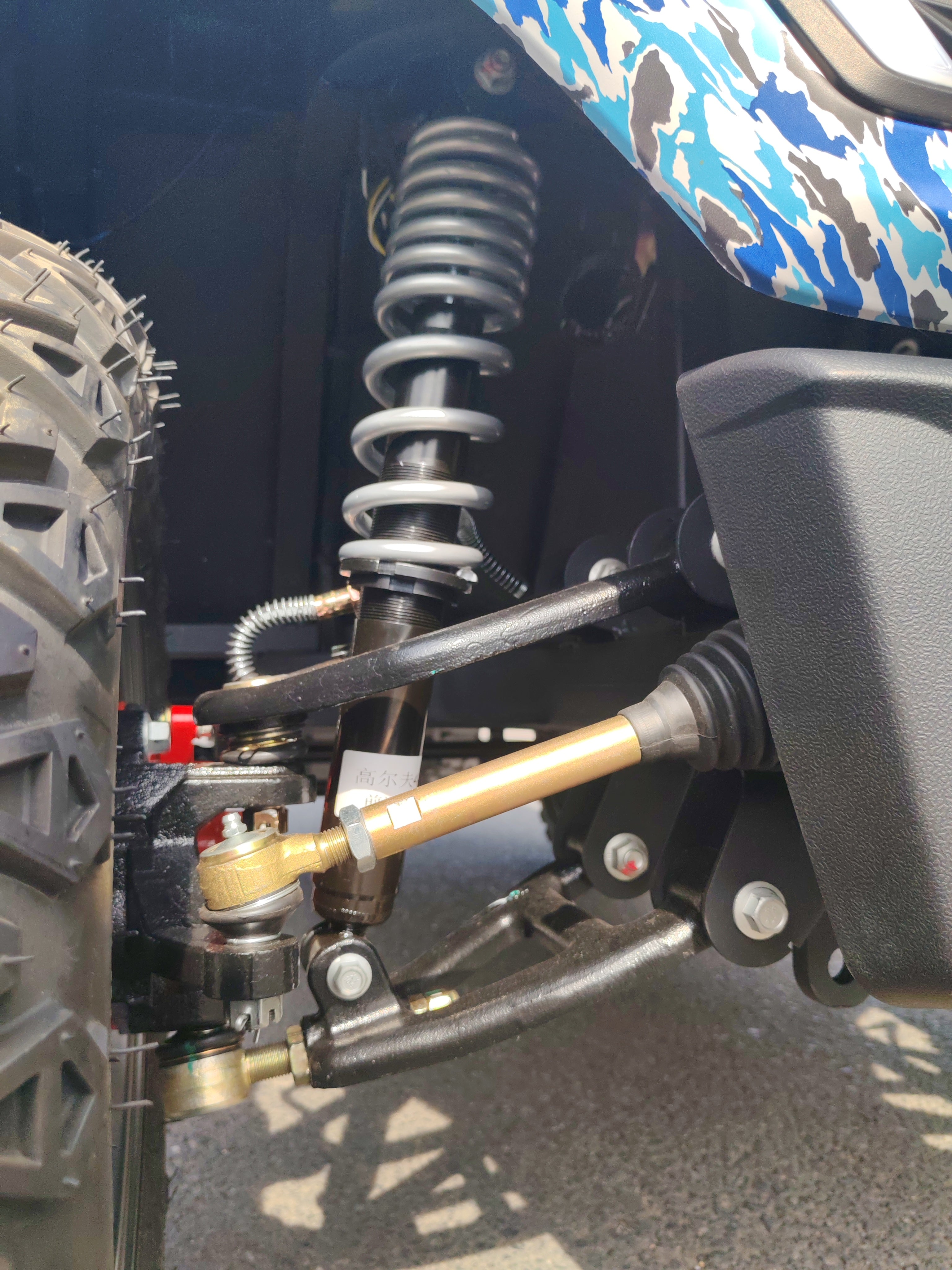 Close-up of a suspension system on an off-road golf cart with a camo-patterned background.